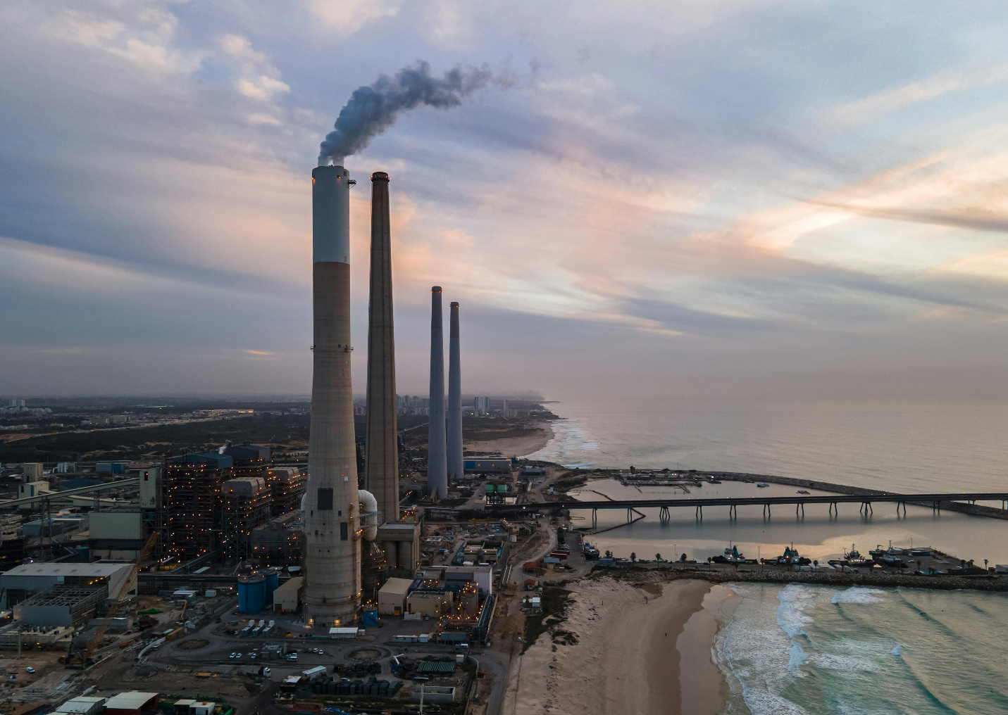 Four large chimneys are seen by the sea as part of a large plant, highlighting the need for critical infrastructure management for regional energy security.