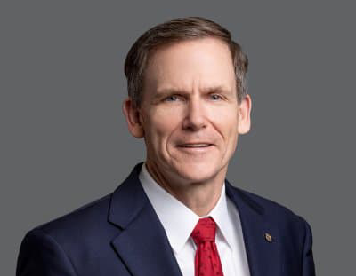 A man in a suit jacket and red tie, against a grey background, Robert (Bob) Herman, Advisory Board Member, ensures operational excellence at Entara